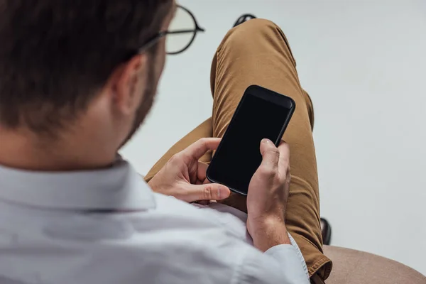 Schnappschuss eines jungen Mannes mit Brille mittels Smartphone mit leerem Bildschirm isoliert auf grau — Stockfoto