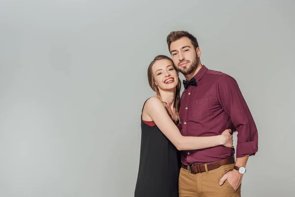 Elegante joven pareja abrazando y sonriendo a la cámara aislada en gris - foto de stock