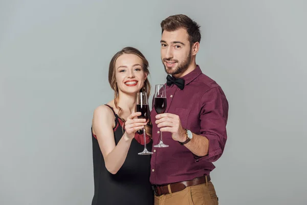 Schöne elegante junge Paar mit Gläsern Rotwein und lächelt in die Kamera isoliert auf grau — Stockfoto
