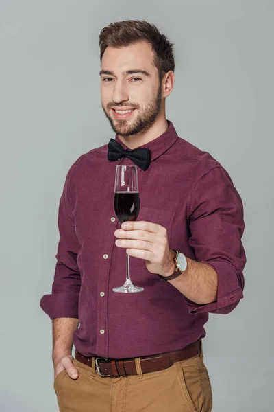 Schöner, stylischer junger Mann mit einem Glas Rotwein und lächelt isoliert in die Kamera auf grau — Stockfoto