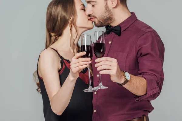 Nahaufnahme von schönen jungen Paar hält Gläser Rotwein und küsst isoliert auf grau — Stockfoto