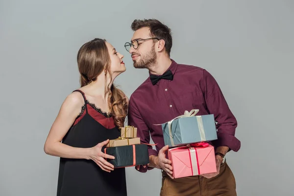 Modisch glückliches junges Paar hält Geschenkboxen in der Hand und kann sich isoliert auf grau küssen — Stockfoto