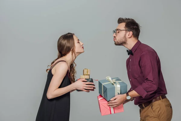 Seitenansicht eines glücklichen jungen Paares, das Geschenkboxen hält und sich isoliert auf grau küssen kann — Stockfoto