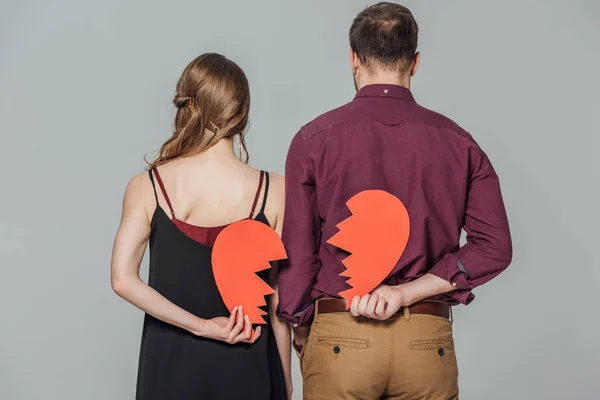 Vista trasera de pareja joven sosteniendo el símbolo del corazón roto aislado en gris - foto de stock