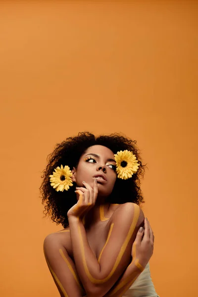 Joven mujer afroamericana sensual con maquillaje artístico y gerbera en pelo aislado sobre fondo naranja — Stock Photo