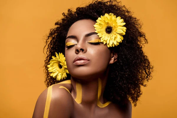 Giovane donna afroamericana sensuale con trucco artistico e gerbera in capelli isolati su sfondo arancione — Foto stock