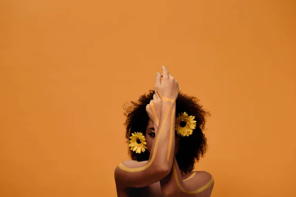Jovem mulher americana africana sensual com maquiagem artística e gerbera no cabelo isolado em fundo laranja — Fotografia de Stock
