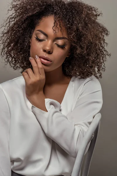 Jeune femme afro-américaine tendre en chemise blanche avec doigt sur les lèvres isolées sur fond gris — Photo de stock