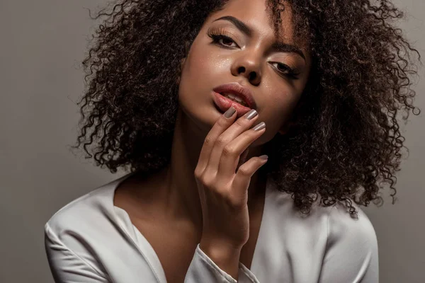 Mujer afroamericana tierna joven en camisa blanca con la mano en los labios aislados sobre fondo gris - foto de stock