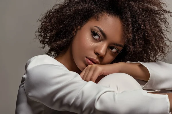 Joven mujer afroamericana sensual en camisa blanca mirando hacia otro lado aislado sobre fondo gris - foto de stock