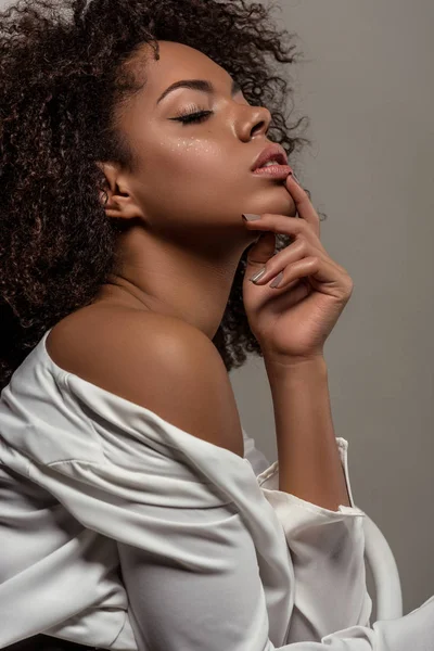 Jovem mulher afro-americana macia em camisa branca sonhando com a mão no queixo isolado em fundo cinza — Fotografia de Stock