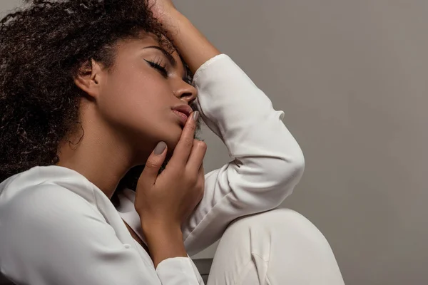 Jeune femme afro-américaine tendre en chemise blanche touchant les lèvres isolées sur fond gris — Photo de stock