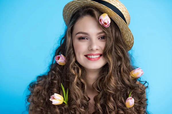 Heureuse jeune femme en chapeau canotier avec des fleurs dans ses longs cheveux bouclés — Photo de stock