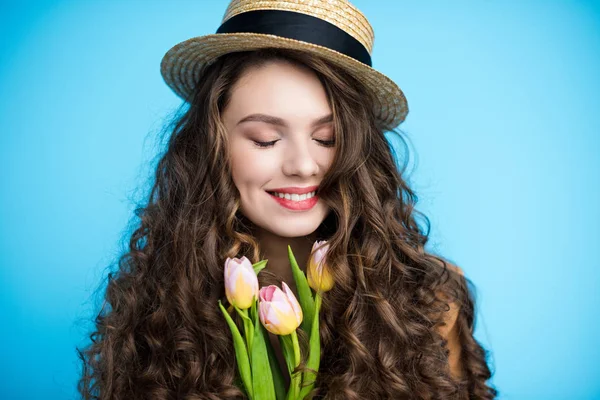 Mujer joven feliz con el pelo rizado largo en sombrero canotier celebración de hermosos tulipanes - foto de stock