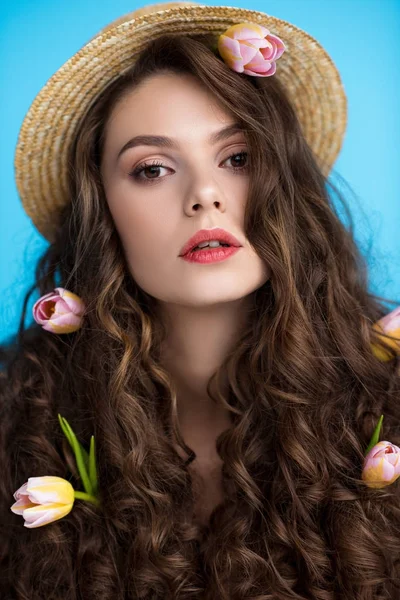 Крупним планом портрет молодої жінки в капелюсі з квітами в її довге кучеряве волосся дивиться на камеру — стокове фото