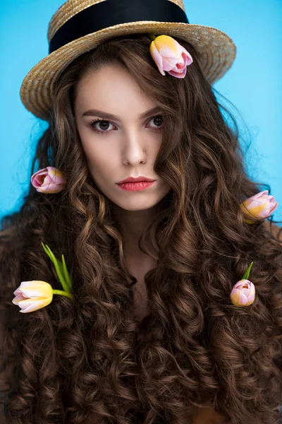 Mujer seria en sombrero canotier con flores en su largo pelo rizado mirando a la cámara - foto de stock