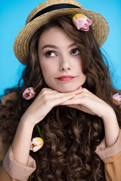 Jeune femme réfléchie en chapeau canotier avec des fleurs dans ses longs cheveux bouclés — Photo de stock
