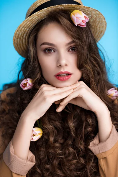 Hermosa mujer joven en sombrero canotier con flores en su largo pelo rizado mirando a la cámara - foto de stock