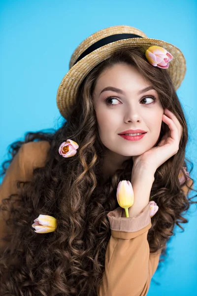 Jeune femme réfléchie en chapeau canotier avec des tulipes dans ses longs cheveux bouclés — Photo de stock