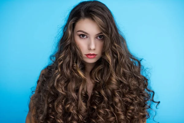 Приваблива молода жінка з довгим кучерявим волоссям ізольована на синьому — стокове фото