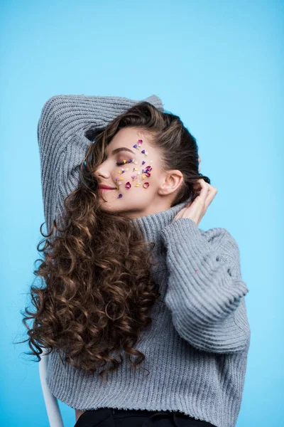 Happy young woman with flower petals on face in sweater isolated on blue — Stock Photo