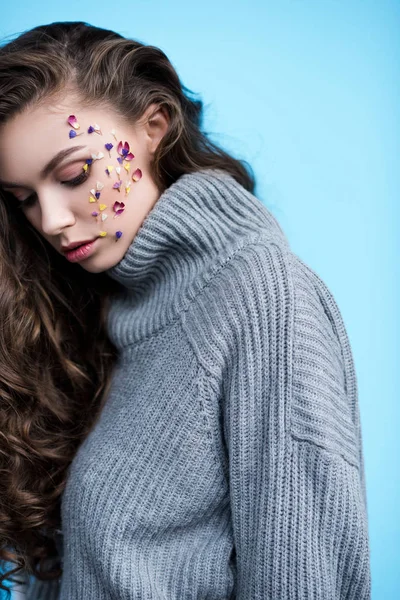 Atractiva joven con flores en la cara en suéter gris cálido aislado en azul - foto de stock