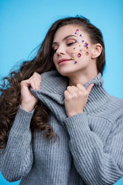 Woman with flowers on face stretching neck of stylish sweater isolated on blue — Stock Photo