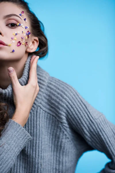 Tiro recortado de mujer en suéter de punto elegante con flores en la cara aislada en azul - foto de stock