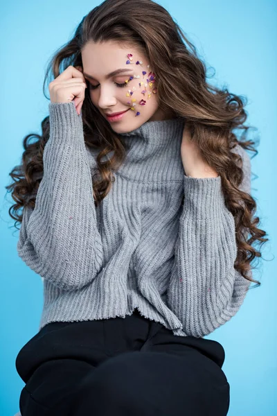 Beautiful smiling brunette woman with flowers on face and closed eyes posing isolated on blue — Stock Photo