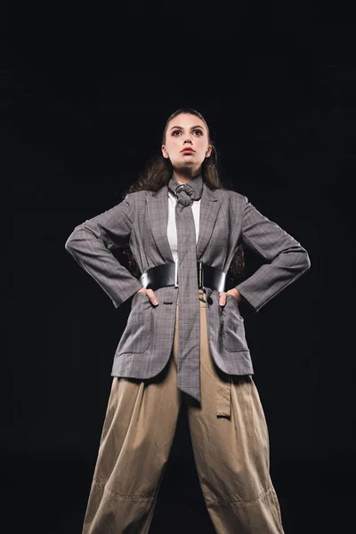 Vue à angle bas de la jeune femme confiante avec les mains sur la taille posant isolé sur noir — Photo de stock