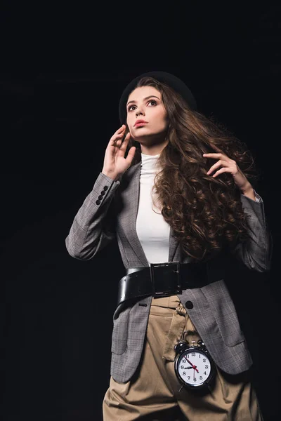 Low angle view of fashionable pensive young woman with clock looking away isolated on black — Stock Photo