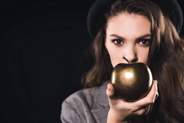 Вид крупним планом молода жінка тримає золоте яблуко і дивиться на камеру ізольовано на чорному — стокове фото