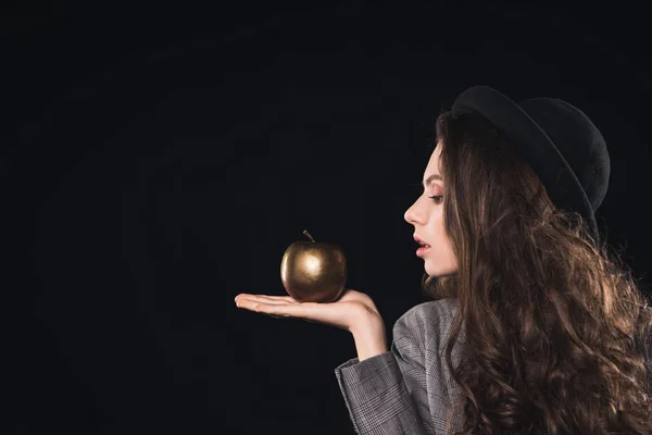 Side view of fashionable young woman holding golden apple on palm isolated on black — Stock Photo