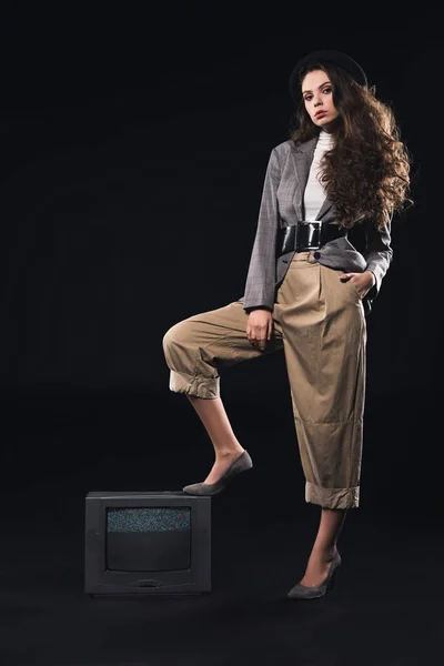 Fashionable woman standing on tv with noises on the screen and looking at camera on black — Stock Photo