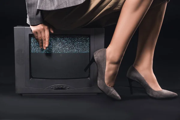 Cropped shot of stylish woman sitting on tv with noises on the screen on black — Stock Photo