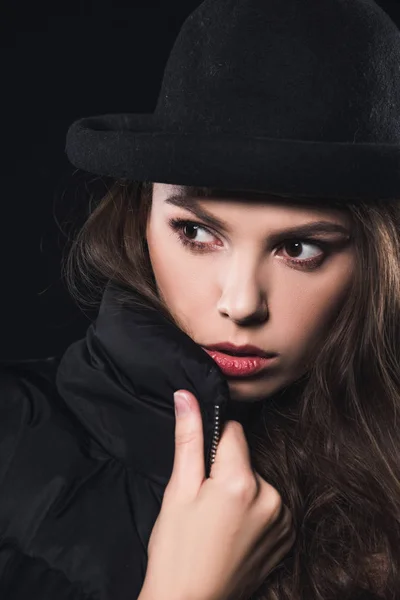 Vista de cerca de la hermosa mujer en sombrero y chaqueta de invierno mirando hacia otro lado aislado en negro - foto de stock