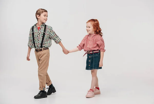 Entzückende kleine Kinder, die sich an den Händen halten und isoliert auf grau laufen — Stockfoto