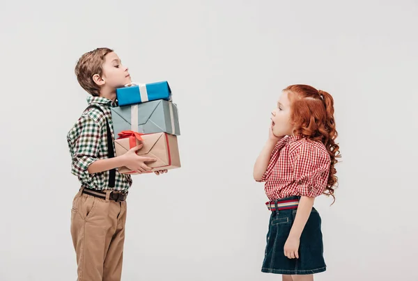 Seitenansicht eines Jungen, der schockierten kleinen Mädchen Geschenke überreicht, isoliert auf grau — Stockfoto