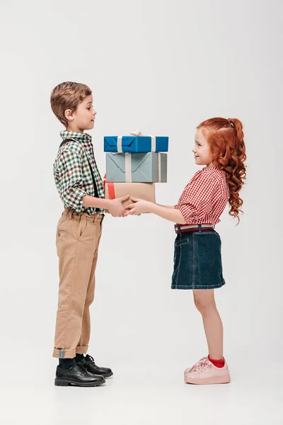 Vista laterale di adorabili bambini felici che tengono i regali isolati sul grigio — Foto stock