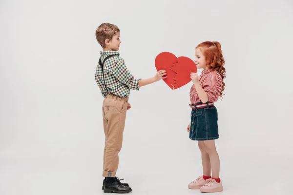 Side view of cute little couple holding parts of broken heart isolated on grey — Stock Photo