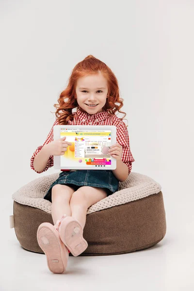 Adorable little girl smiling at camera while holding digital tablet with aliexpress website on screen isolated on grey — Stock Photo