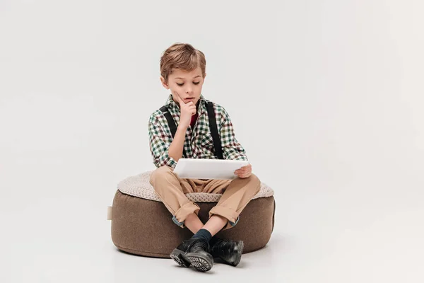 Зосереджений маленький хлопчик сидить і використовує цифровий планшет ізольований на сірому — стокове фото