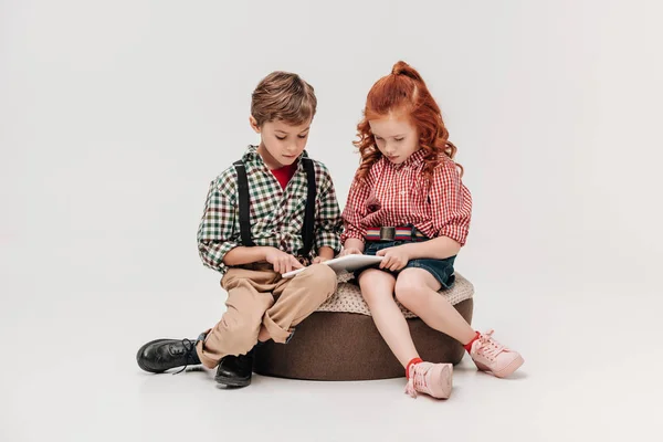 Hermosos niños pequeños usando tableta digital juntos aislados en gris - foto de stock