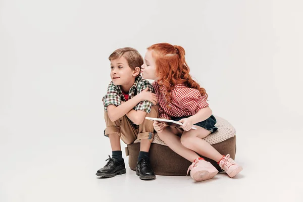 Adorable little girl holding digital tablet and able to kiss little boy isolated on grey — Stock Photo