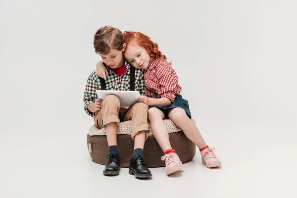 Чарівні діти, що обіймаються і використовують цифровий планшет разом ізольовані на сірому — стокове фото