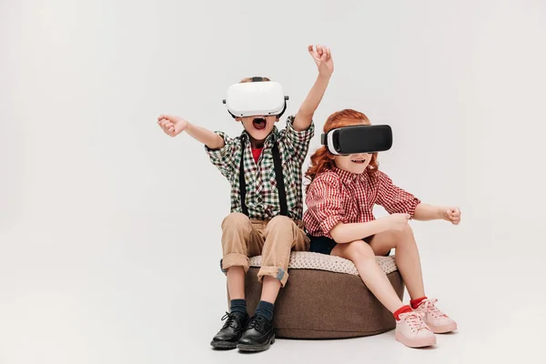 Прелестные маленькие дети, играющие в наушниках виртуальной реальности, изолированных на сером — стоковое фото