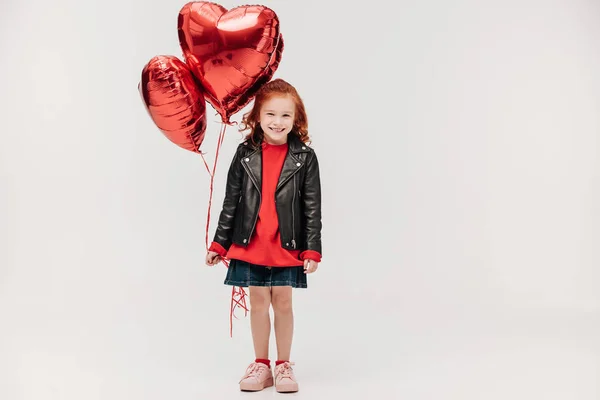 Щаслива дівчинка з повітряними кулями у формі сердець ізольована на сірому — стокове фото