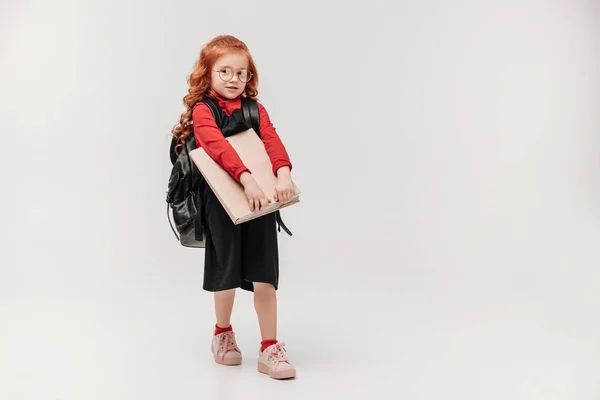 Adorable little schoolgirl in black dress with big book isolated on grey — Stock Photo