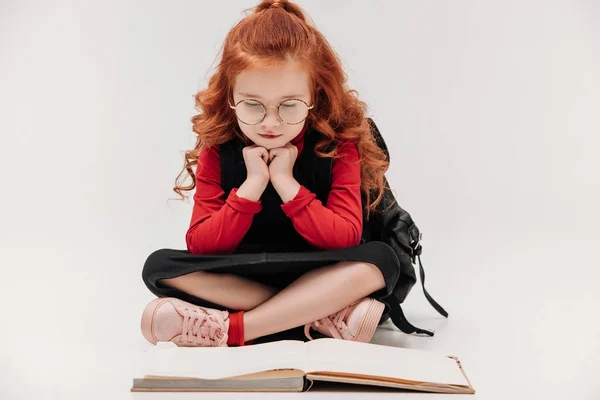 Adorable little schoolgirl reading book on floor isolated on grey — Stock Photo