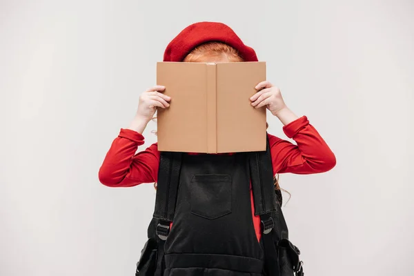 Pequena estudante cobrindo rosto com livro isolado em cinza — Fotografia de Stock